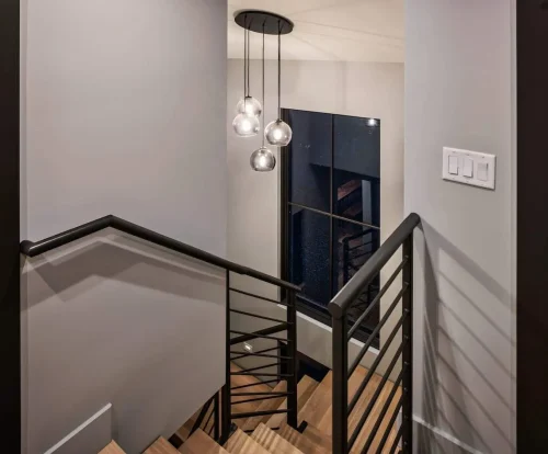 Upper stairwell with modern black railing and hanging pendant lights, accented by a tall window.