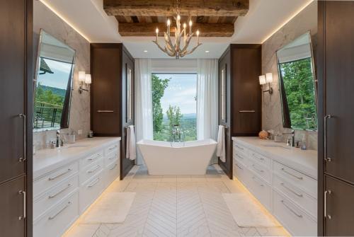 Rustic Mountain Estate white bathroom with modern porcelain tub under window and deer antler chandelier.