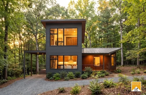 Side view of a modern wooded home with dark siding, tall illuminated windows, an elevated deck, and a gravel driveway.