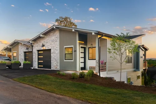 Contemporary home with stone and siding exterior, sloped rooflines, an attached garage, and covered entry.