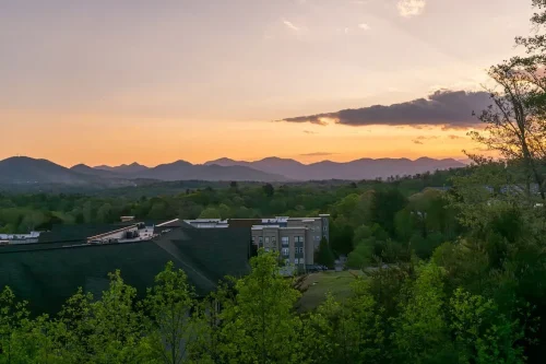 Panoramic sunset view of layered mountain ridges above the surrounding community and trees.