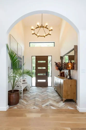Welcoming foyer with a wood front door, herringbone tile floor, rustic sideboard, and natural light from a clerestory window.