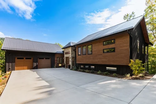 Contemporary mountain home exterior with dark siding, wood accents, and stone entry, featuring a spacious driveway and two-car garage.