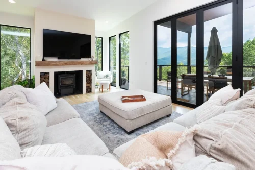 Cozy living room with a large sectional sofa, wood-burning fireplace with TV above, and sliding doors opening to a deck with mountain views.