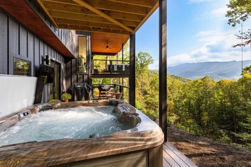 Covered lower deck featuring a hot tub overlooking the Blue Ridge Mountains, with outdoor seating and grill area nearby.