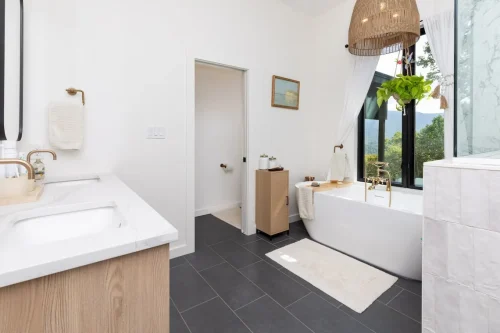 Spa-inspired owner’s bathroom with a freestanding tub, gold fixtures, woven pendant light, and large windows framing mountain views.