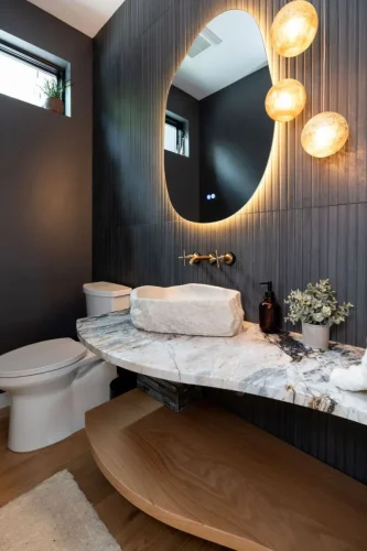Stylish powder room with a natural stone vessel sink, marble countertop, dark textured walls, and a modern backlit mirror.