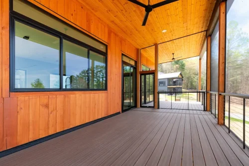 Covered porch with natural wood siding, black trim, ceiling fan, and wide glass doors leading into the home.