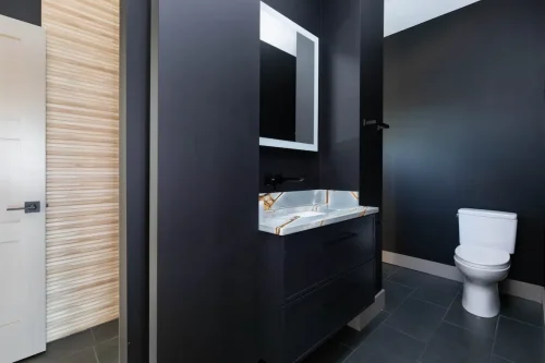 Compact bathroom with dark walls, floating vanity, marble counter, illuminated mirror, and modern fixtures.