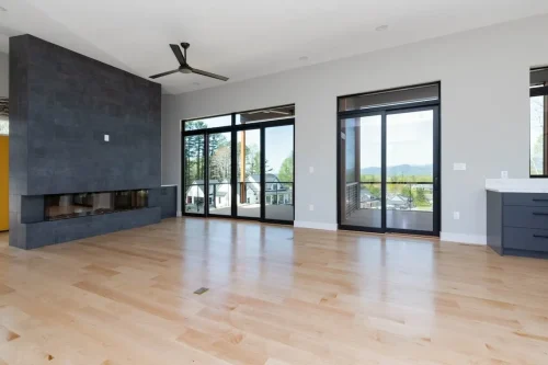 Modern living room with light hardwood flooring, dark tiled fireplace wall, and oversized windows showcasing mountain views.