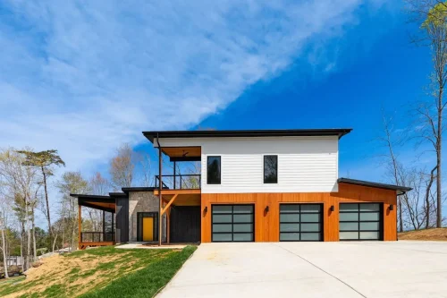 Contemporary mountain home with wood, stone, and white siding accents, black framed windows, and multi-car garage.