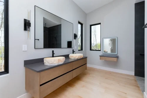 Luxury bathroom with floating double vanity, stone vessel sinks, large mirror, and sleek lighting beside black-tiled walk-in shower.